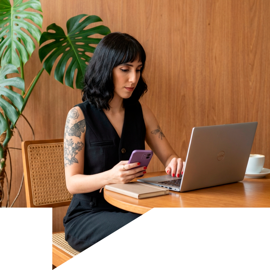 Mulher moderna sentada em uma cafeteria trabalhando com criação de site em um laptop cinza e usando um celular - criativo site